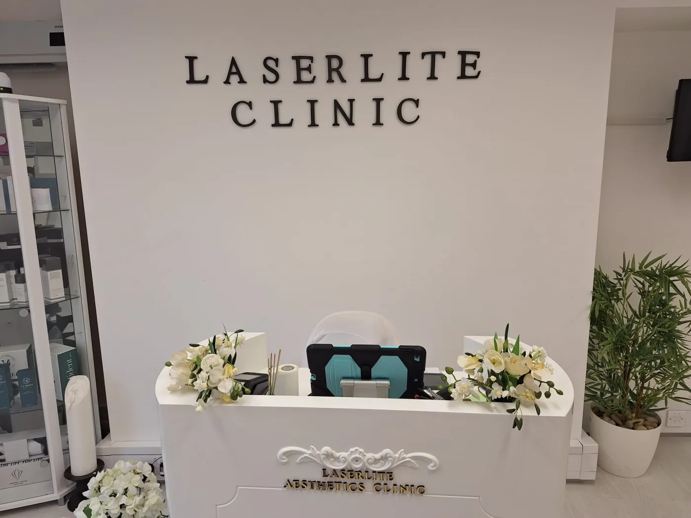 The Laserlite Clinic reception desk with fresh flowers, under the clinic lettering The Laserlite Clinic reception desk with fresh flowers, under the clinic lettering