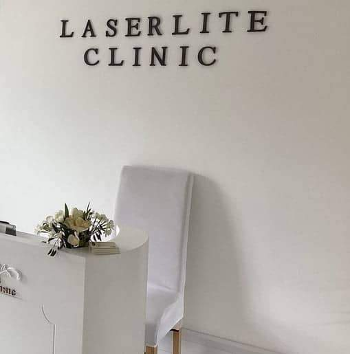 The clinic's reception, with LASERLITE CLINIC lettering on the wall, a white desk with flowers and a chair The clinic's reception, with LASERLITE CLINIC lettering on the wall, a white desk with flowers and a chair