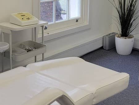 A calm treatment room with a sash window, a tall plant and a treatment trolley A calm treatment room with a sash window, a tall plant and a treatment trolley